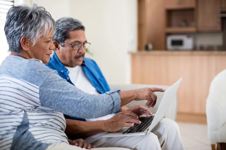 Senior couple sitting on sofa looking at laptop computer held in the man's lap.